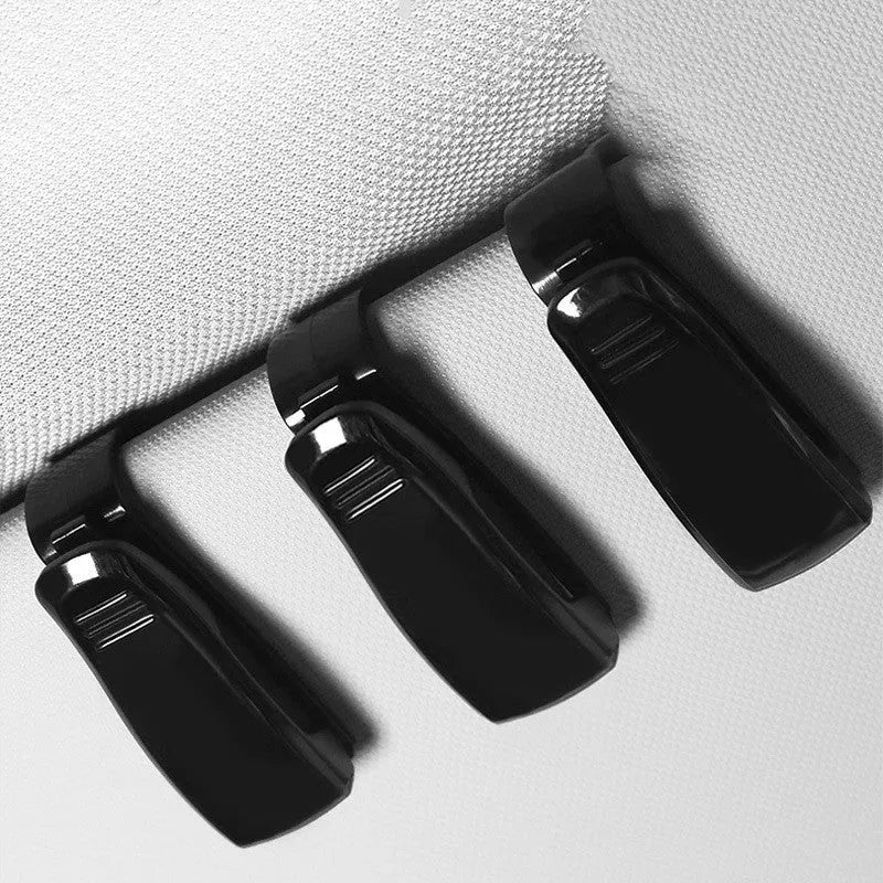 Black plastic clip for car sunshade holding sunglasses and a ticket.