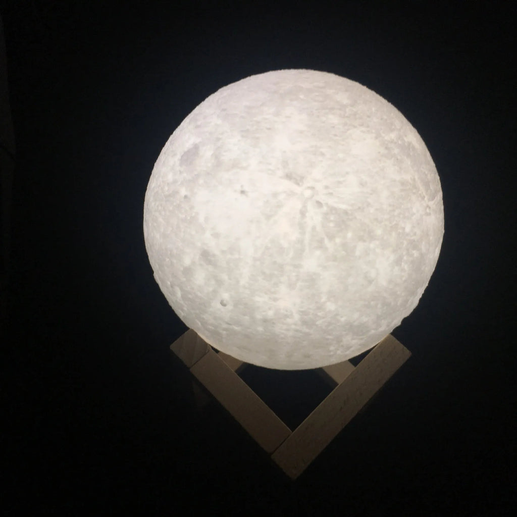 3D printed white moon lamp glowing on a wooden stand, showing detailed lunar craters.