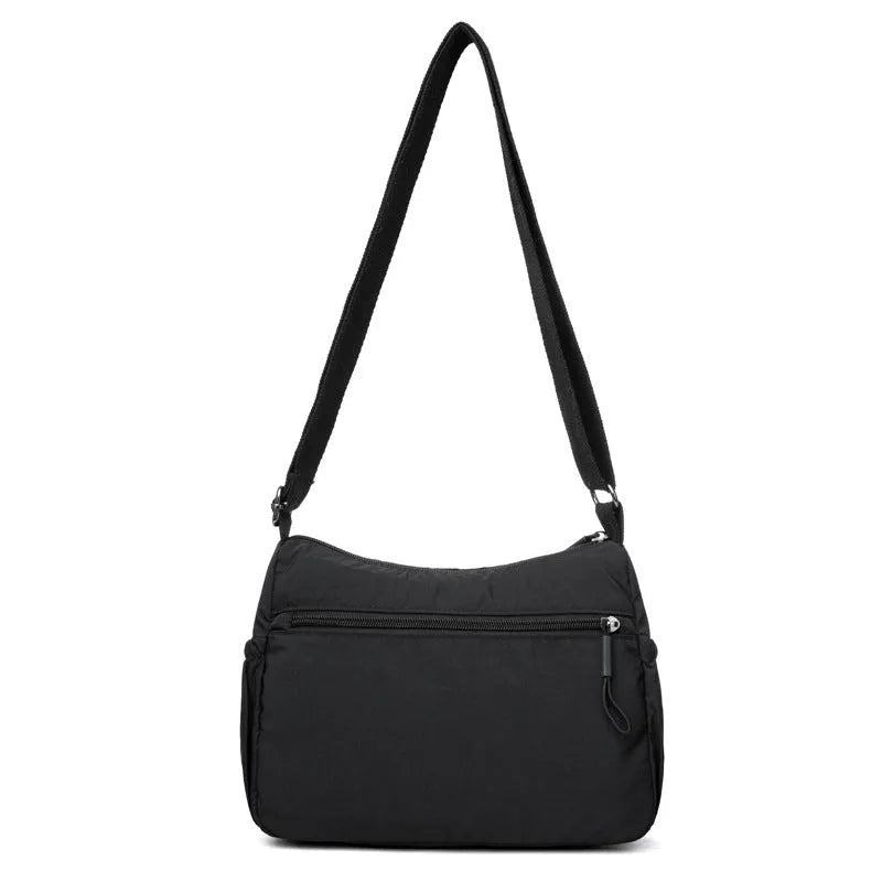 Soft water-repellent nylon crossbody bag in black, grey, or red, showing interior zipper pockets and an exterior 3D pocket.