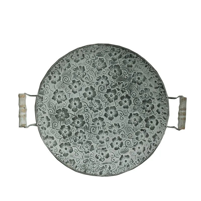 Round wrought iron belt storage tray with raised rim in two sizes on a wooden table.