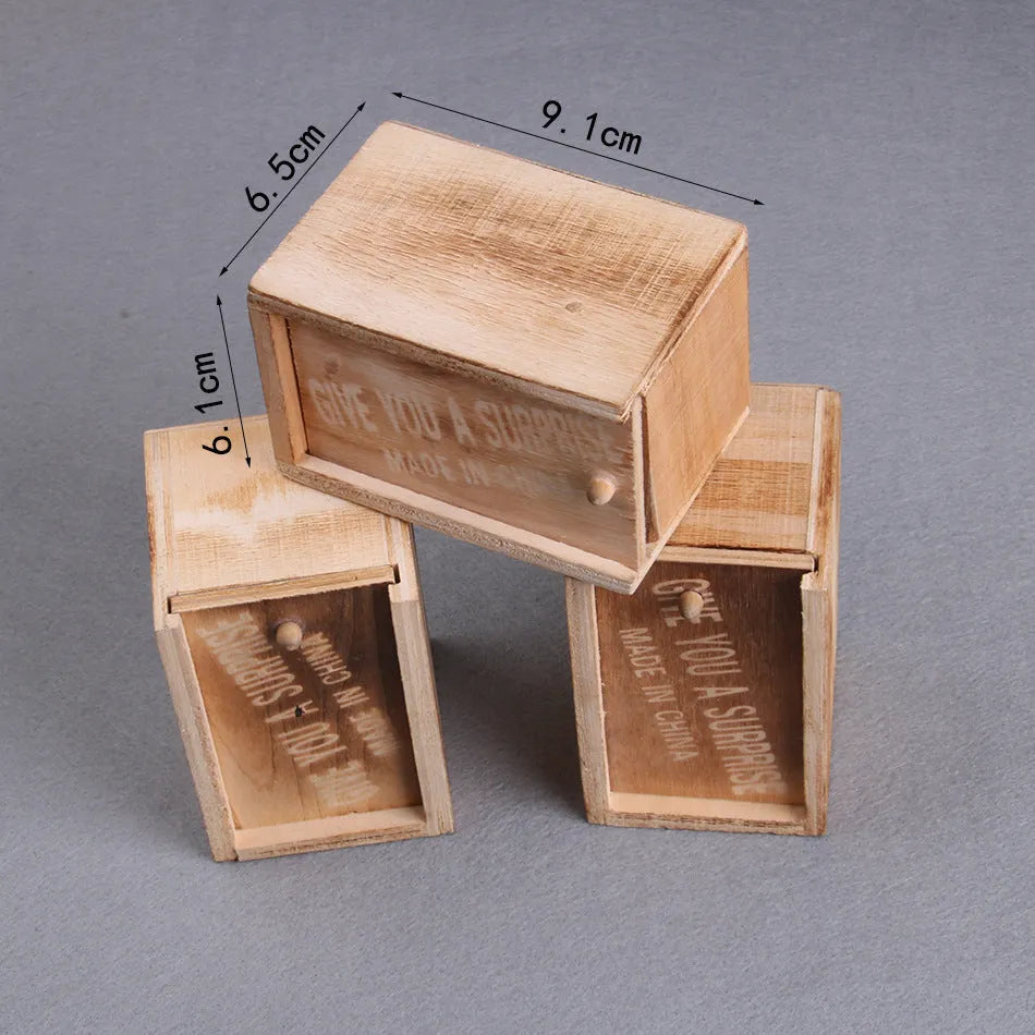 Wooden prank box with lid open showing a lifelike jumping spider inside on a white background.