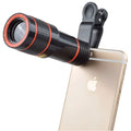 A black 12X phone telescope lens next to a universal mounting clip and cleaning cloth on a table.