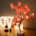 White and red rose flower LED table lamp with bonsai tree and garland lights on a table.