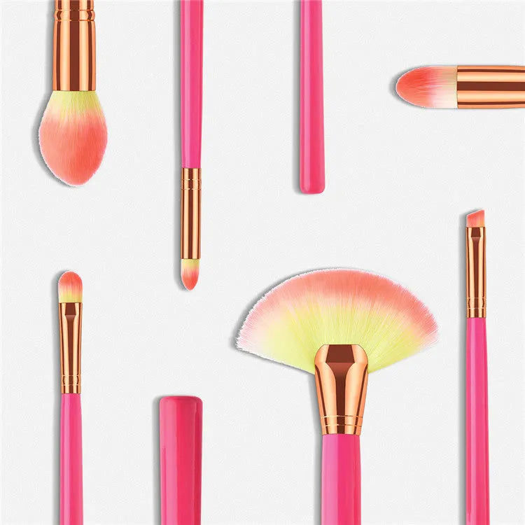 Pink cosmetic makeup brush set with wooden handles and synthetic bristles laid out on a surface