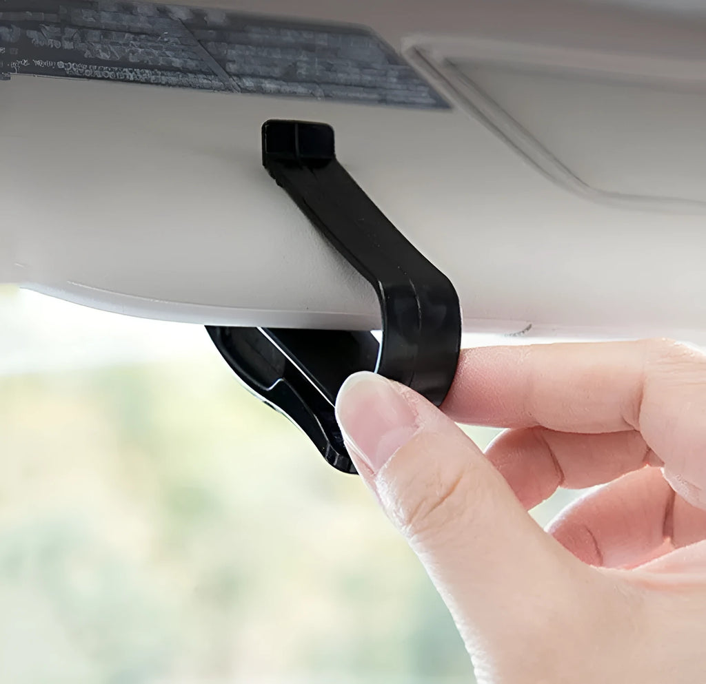 Black plastic clip for car sunshade holding sunglasses and a ticket.