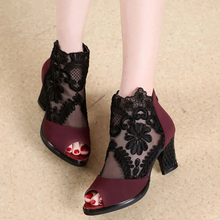 Black lace gladiator sandals with a square high heel, zip closure, and peep toe on a woman's foot