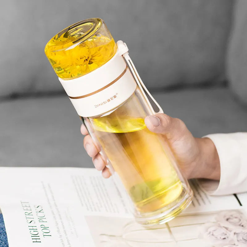 Green double-wall glass water bottle with tea infuser, stainless steel filter, and rope handle on a wooden table.