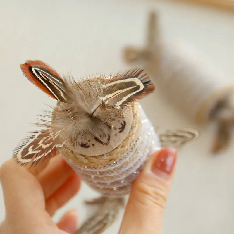 Beige cat toy with hemp rope scratching post, feathers, and a built-in sound roller on a neutral background.