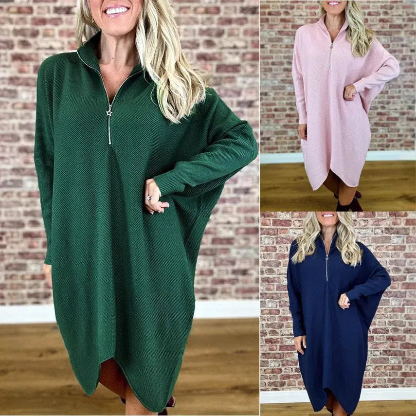 A woman wearing a solid dark green loose-fit knitted dress with raglan sleeves and a zipper detail.