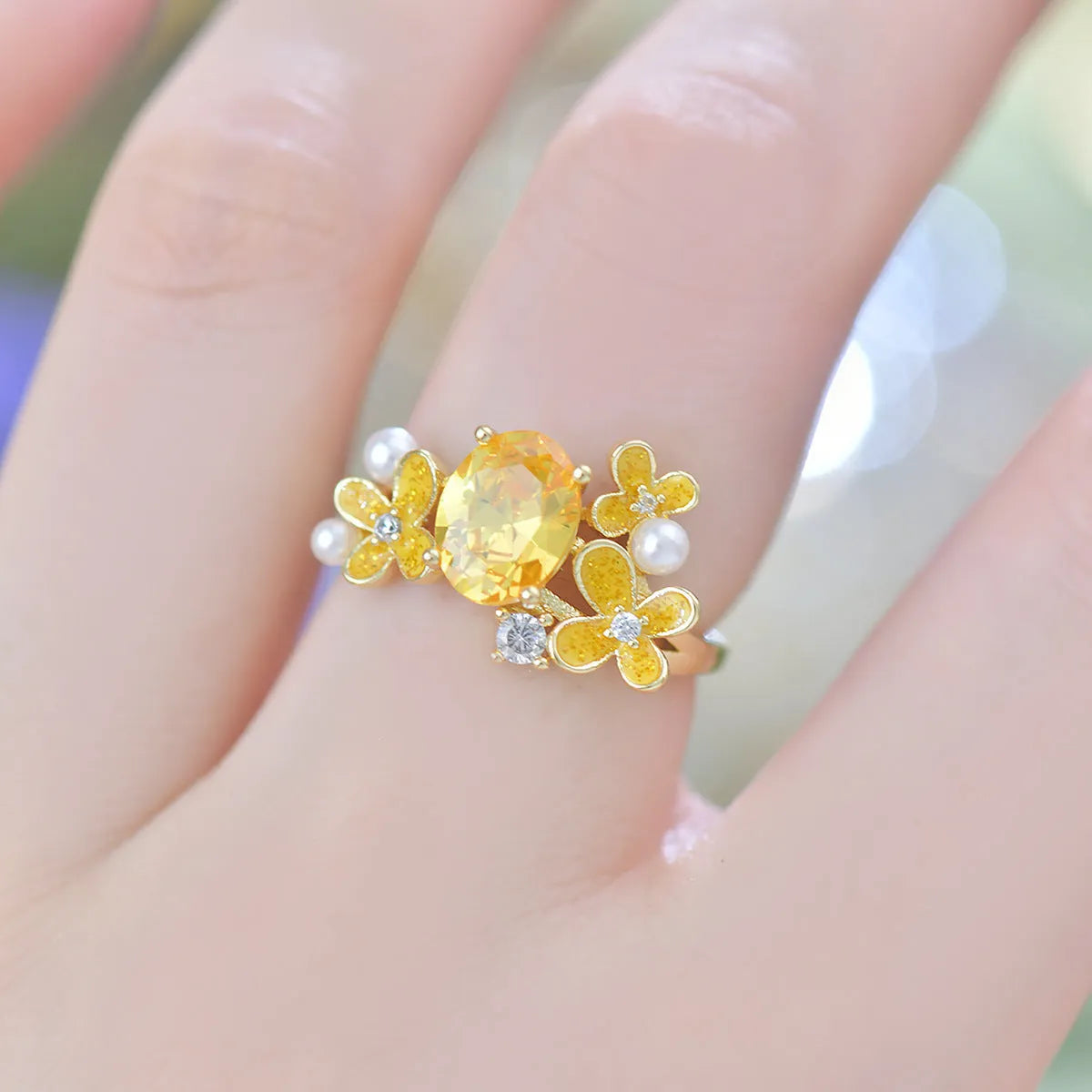 Yellow women's open ring with a flower shape and zircon detailing on a white background.