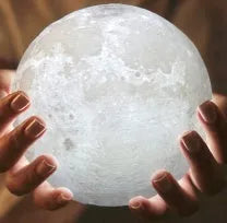3D printed white moon lamp glowing on a wooden stand, showing detailed lunar craters.