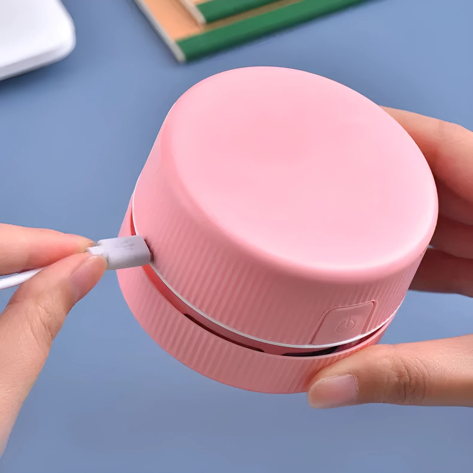 Blue rechargeable mini handheld desktop vacuum cleaner on a wooden desk next to pencils