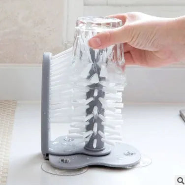 Grey rotating cup brush with two suction cups for wall mounting, shown cleaning a glass