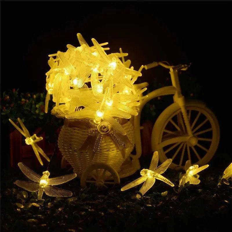 Outdoor solar-powered dragonfly LED string lights with panel on spike in a garden setting