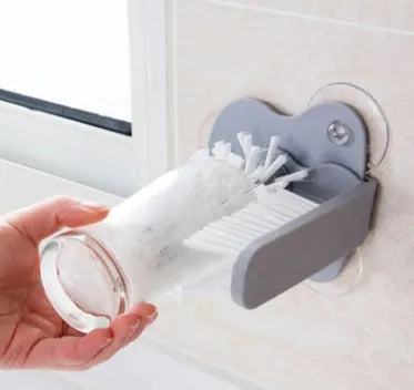Grey rotating cup brush with two suction cups for wall mounting, shown cleaning a glass