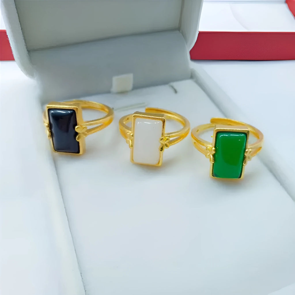 Adjustable brass gold-plated ring with a central green gemstone inlay on a finger.