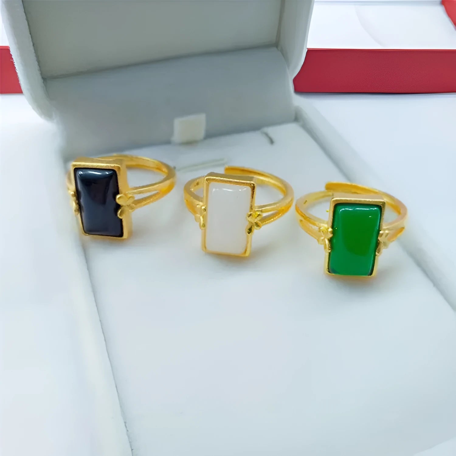 Adjustable brass gold-plated ring with a central green gemstone inlay on a finger.