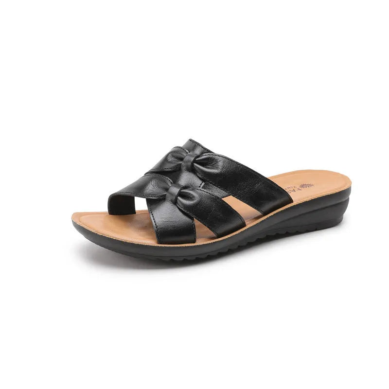 Beige cowhide leather women's slippers with a non-slip sole on a wooden floor.