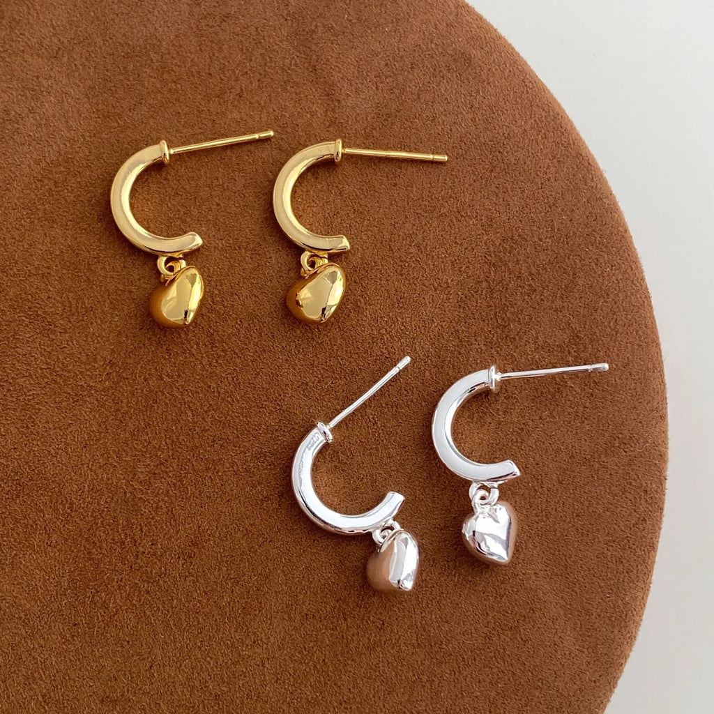 Gold copper C-shaped heart pendant earrings on white background