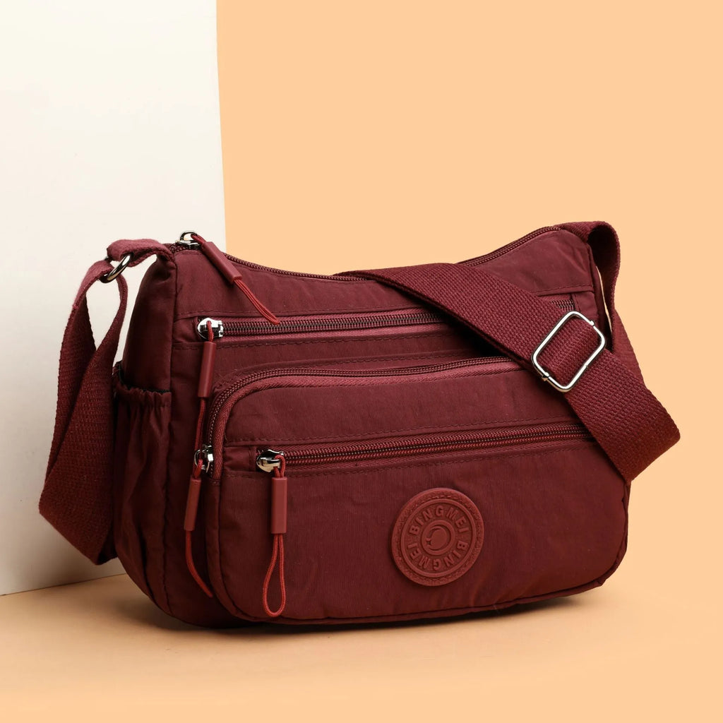 Soft water-repellent nylon crossbody bag in black, grey, or red, showing interior zipper pockets and an exterior 3D pocket.