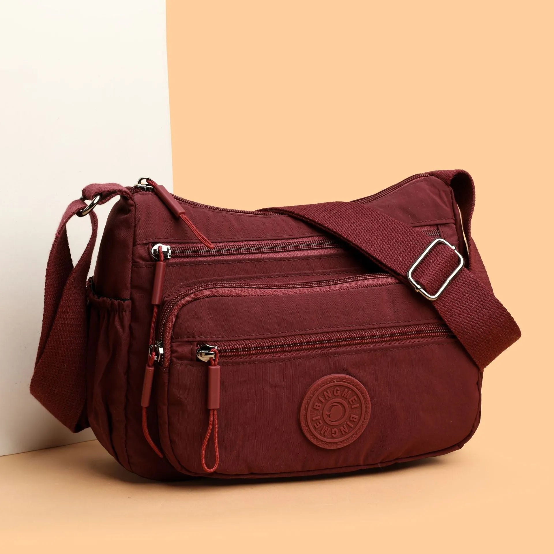 Soft water-repellent nylon crossbody bag in black, grey, or red, showing interior zipper pockets and an exterior 3D pocket.