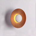 A round, modern wall lamp with an aluminium shade, shown in a two-tone gold and white finish, mounted on a wall.