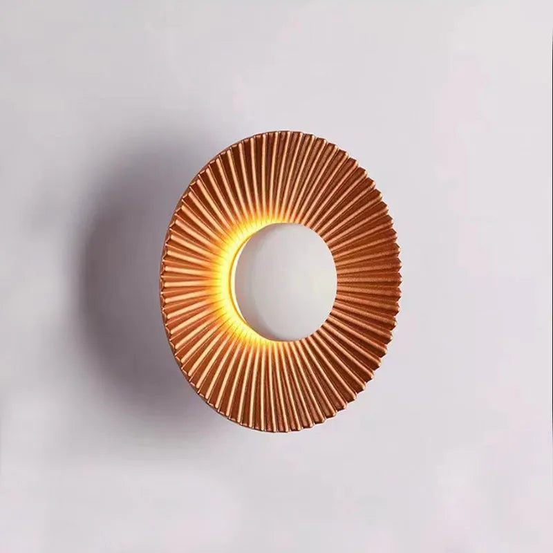 A round, modern wall lamp with an aluminium shade, shown in a two-tone gold and white finish, mounted on a wall.