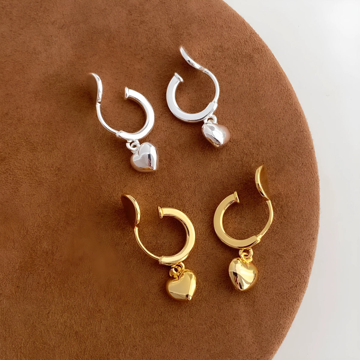 Gold copper C-shaped heart pendant earrings on white background