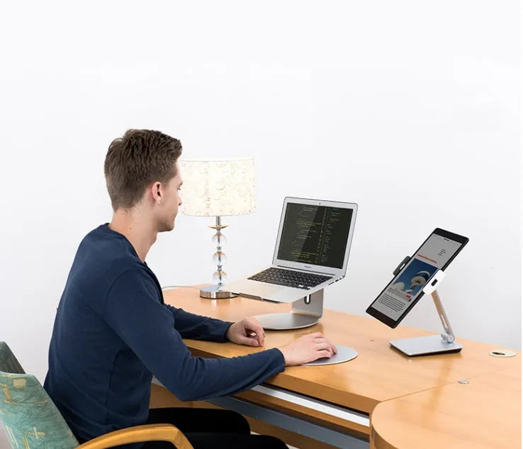 Silver foldable aluminium and ABS phone and tablet stand on a desk, showing 360-degree rotation.