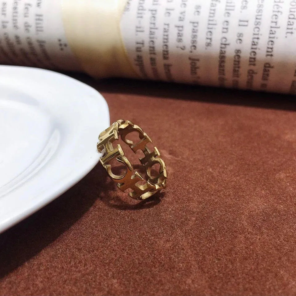 Gold titanium steel hollowed cut letter ring with geometric design on white background