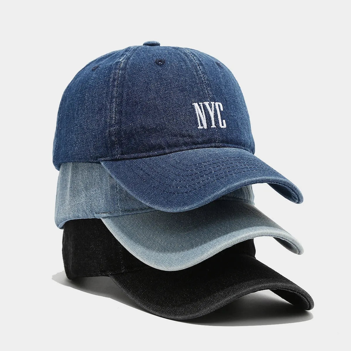Light blue denim peaked cap with embroidered letters on a dome crown, showing adjustable strap.