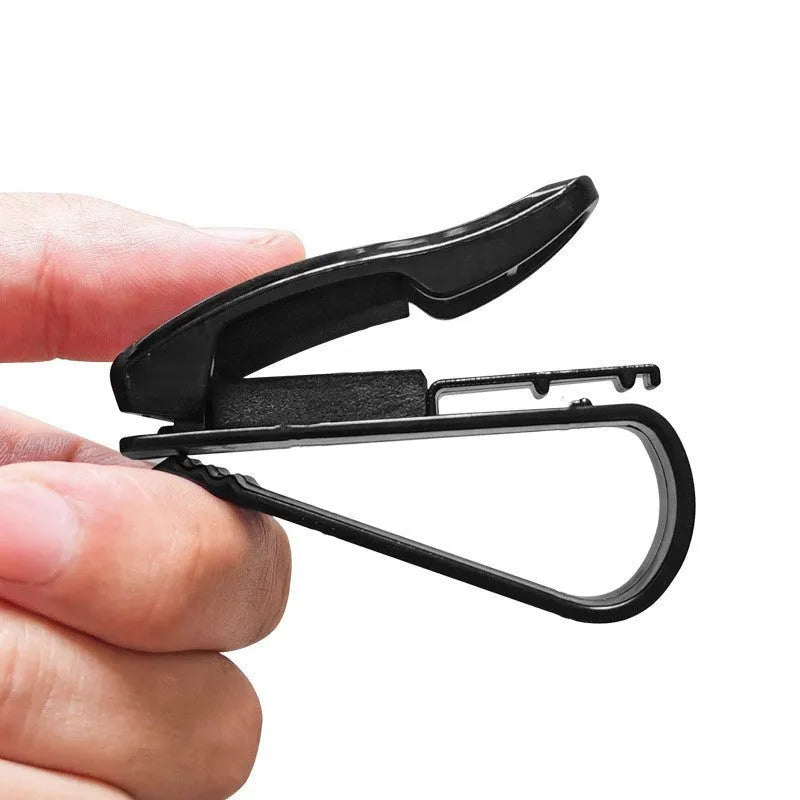 Black plastic clip for car sunshade holding sunglasses and a ticket.
