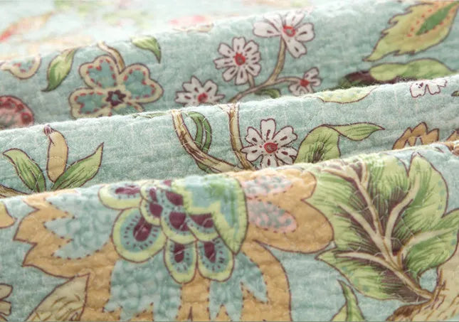 Blue American floral and bird patterned cotton quilted bedspread set on a bed, showing the 230x250 cm size
