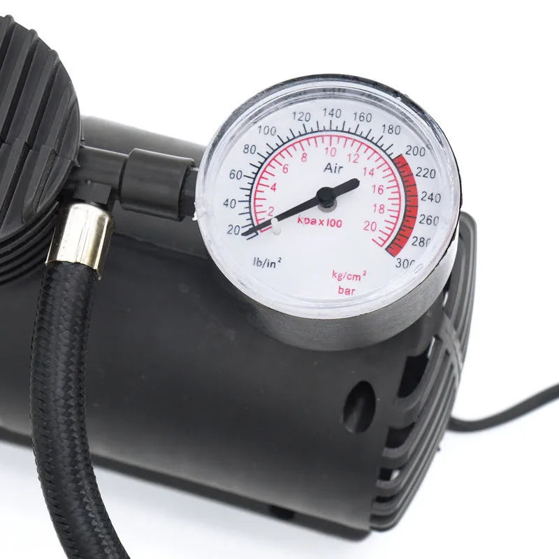 Black portable 12V mini car air compressor with pressure gauge, hose, and two nozzle adapters on grey background