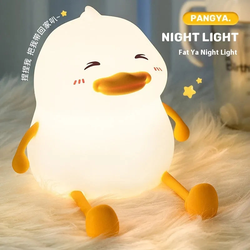 Chubby white silicone night light on a desk holding a mobile phone, showing touch controls and USB port.