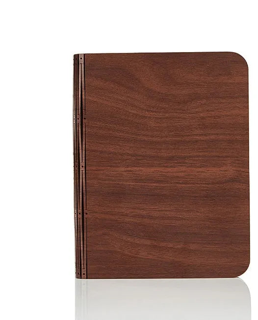 A solid wood adjustable LED book light on a desk next to a book.