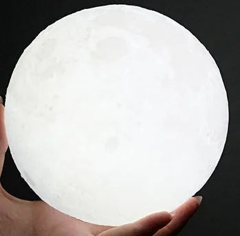 3D printed white moon lamp glowing on a wooden stand, showing detailed lunar craters.