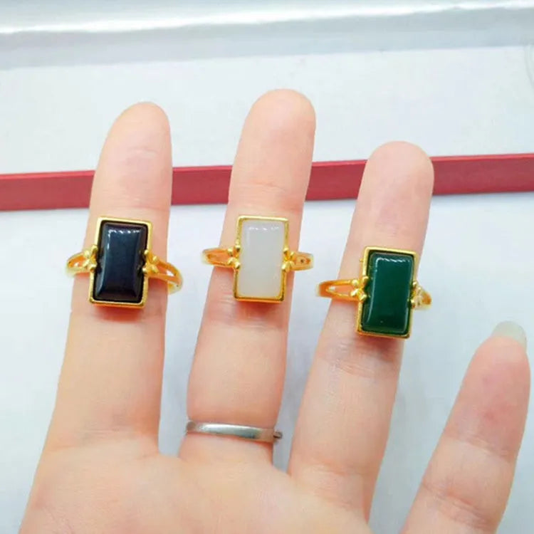 Adjustable brass gold-plated ring with a central green gemstone inlay on a finger.