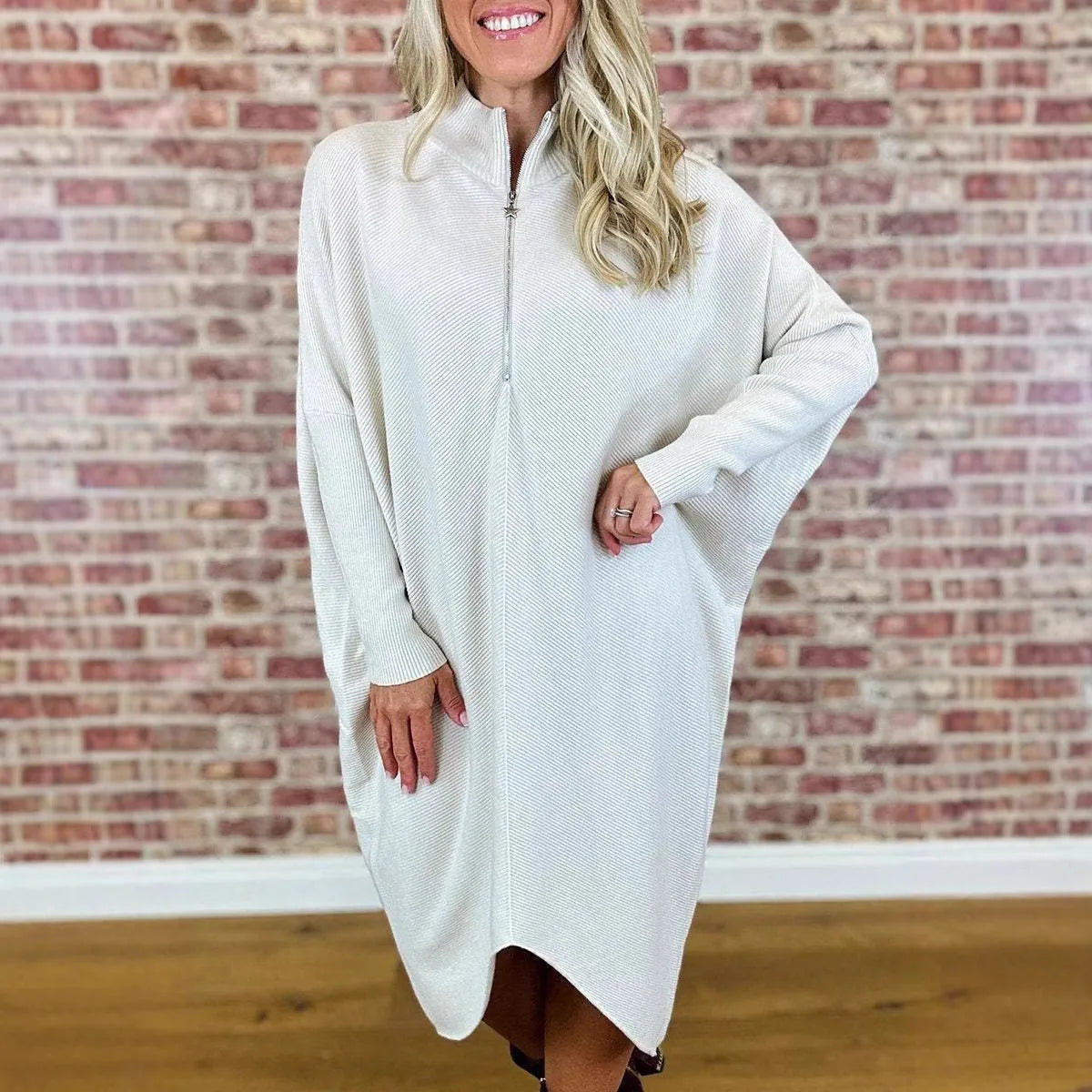 A woman wearing a solid dark green loose-fit knitted dress with raglan sleeves and a zipper detail.