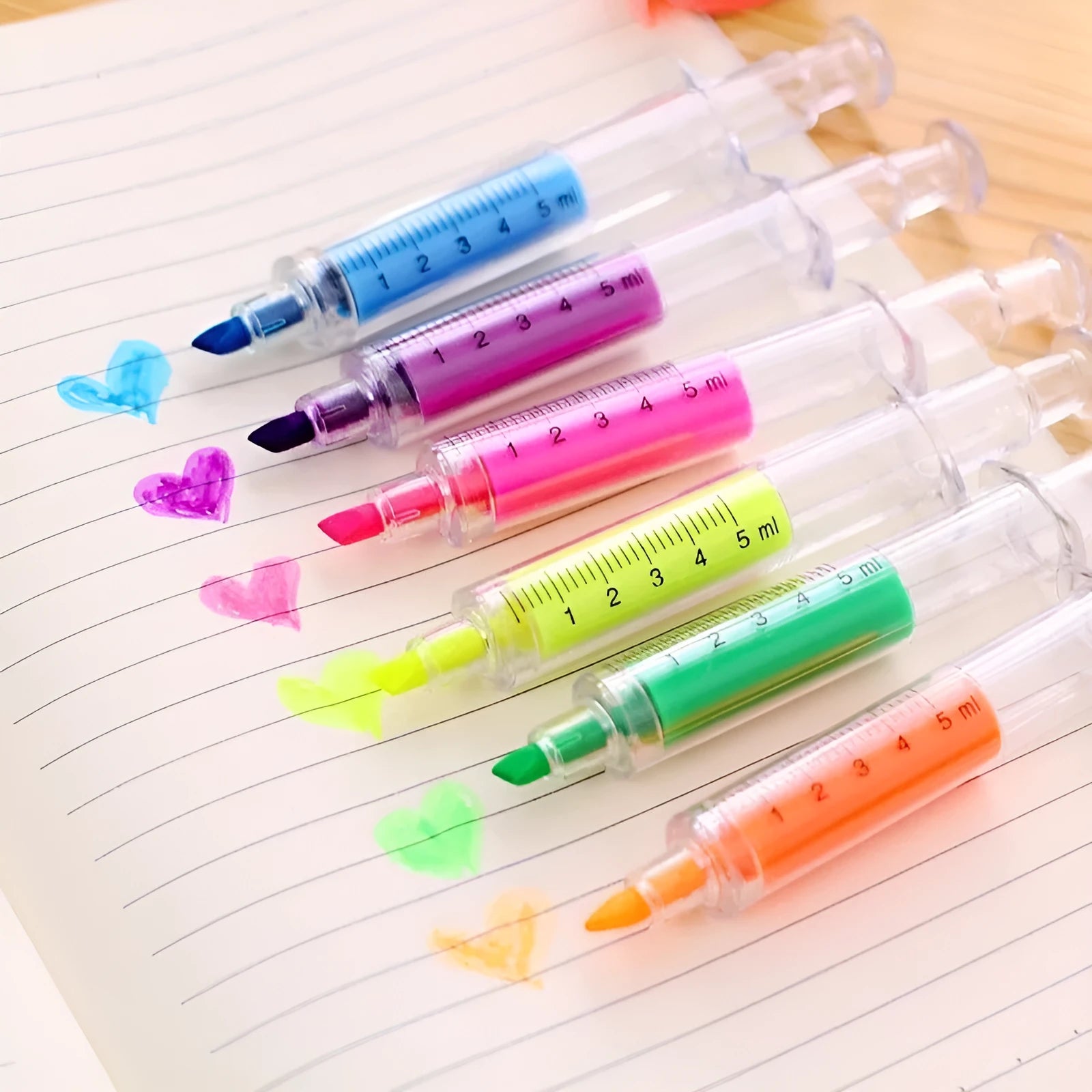 Six syringe-shaped fluorescent highlighter pens in assorted colours on a white background