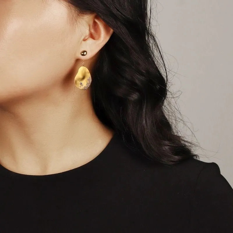 A pair of asymmetric gold-plated flower earrings with zircon detail, shown in silver and gold colour options.