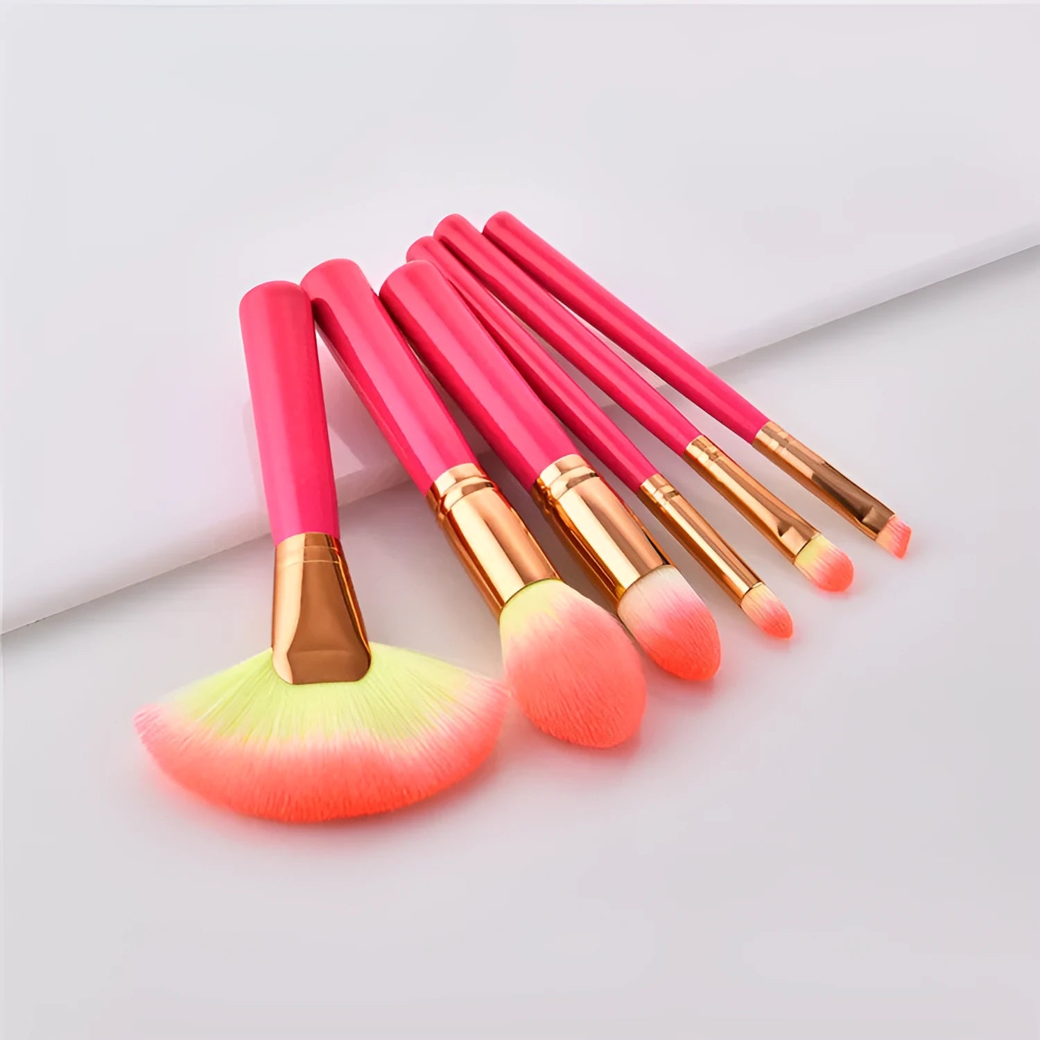 Pink cosmetic makeup brush set with wooden handles and synthetic bristles laid out on a surface