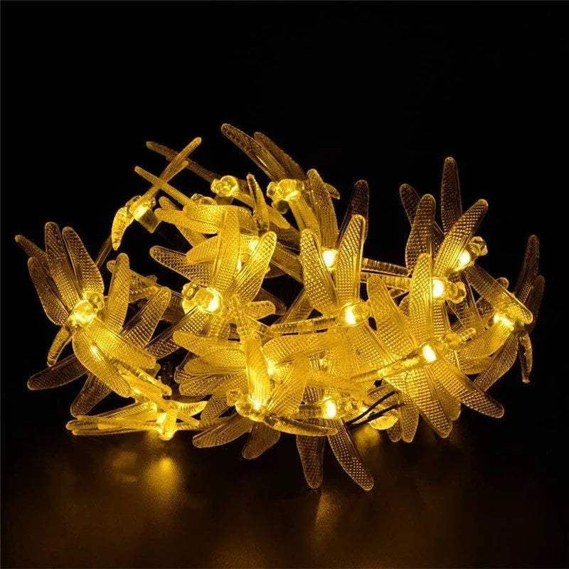 Outdoor solar-powered dragonfly LED string lights with panel on spike in a garden setting