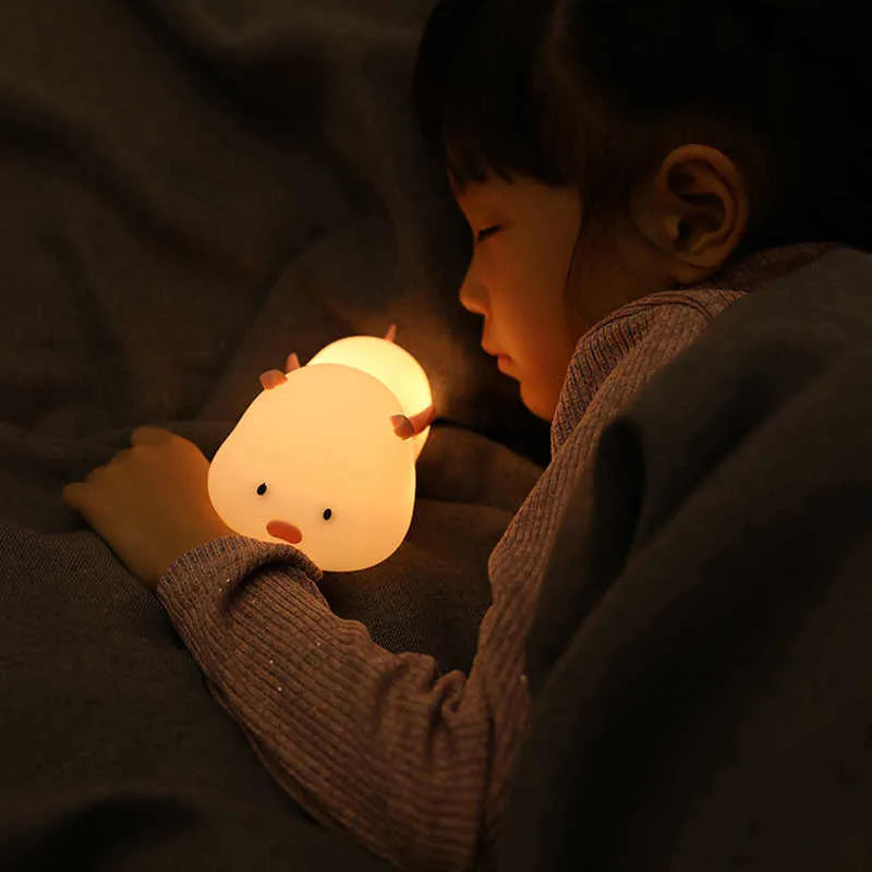 Blue rechargeable pig-shaped silicone night light with a sleeping design on a bedside table.
