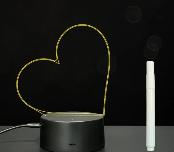 Black 3D acrylic message board lamp with remote control and marker pen on a desk.