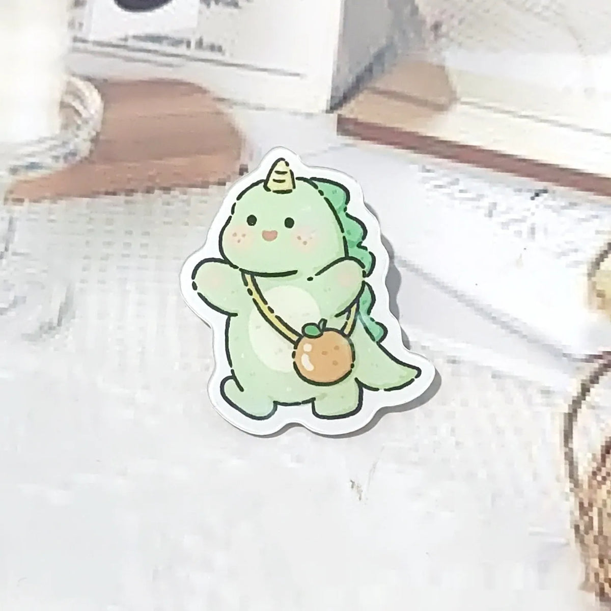 Cartoon dinosaur acrylic badge brooch with printed design and pin fastening, shown in one of twelve colour styles