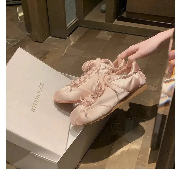 Women's silver satin ballet flats with round toe and white front lace-up on a rubber sole.