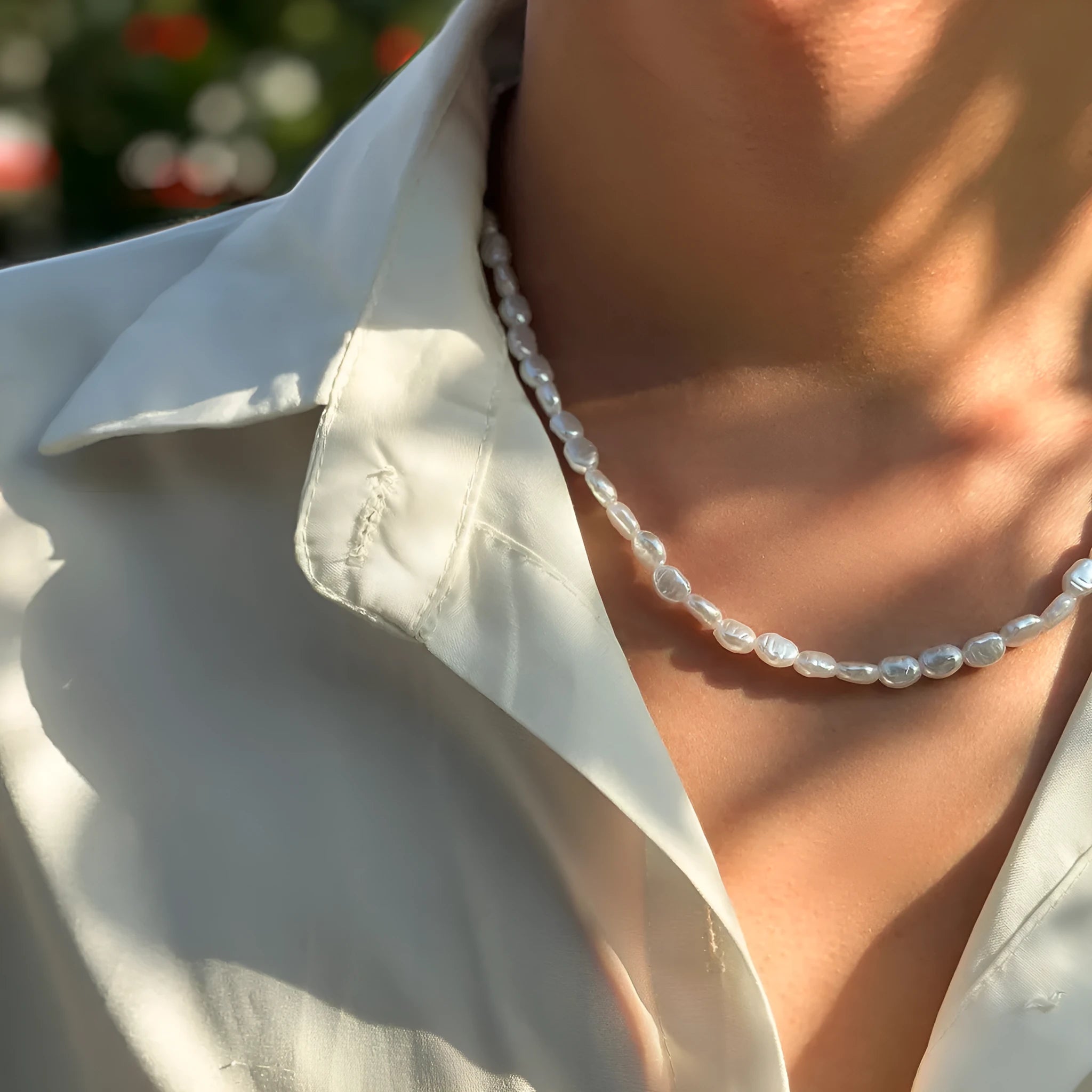 White U-shaped imitation pearl men's necklace with a shellfish pendant on a model.