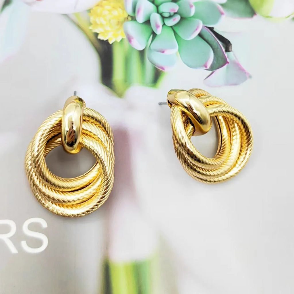 Geometric ring embossed twisted metal stud earrings in gold colour on a plain background