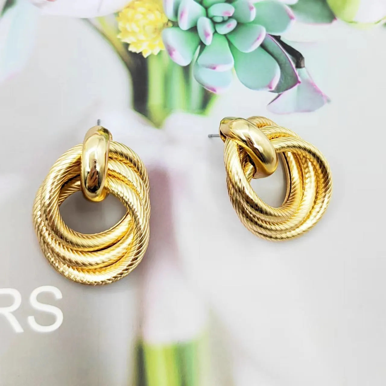 Geometric ring embossed twisted metal stud earrings in gold colour on a plain background